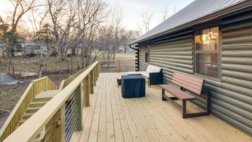 A wooden deck with a bench and table, a railing, and a log cabin in the background.
