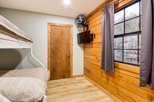 Una habitación con literas, una pared de madera, una ventana con cortinas y un ventilador de techo.