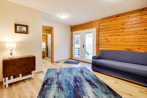 A living room with a wooden wall, a gray sofa, a wooden console table with a lamp, and a blue rug. - Tranquil Creekside Hideout: Families Welcome! (Pineville)