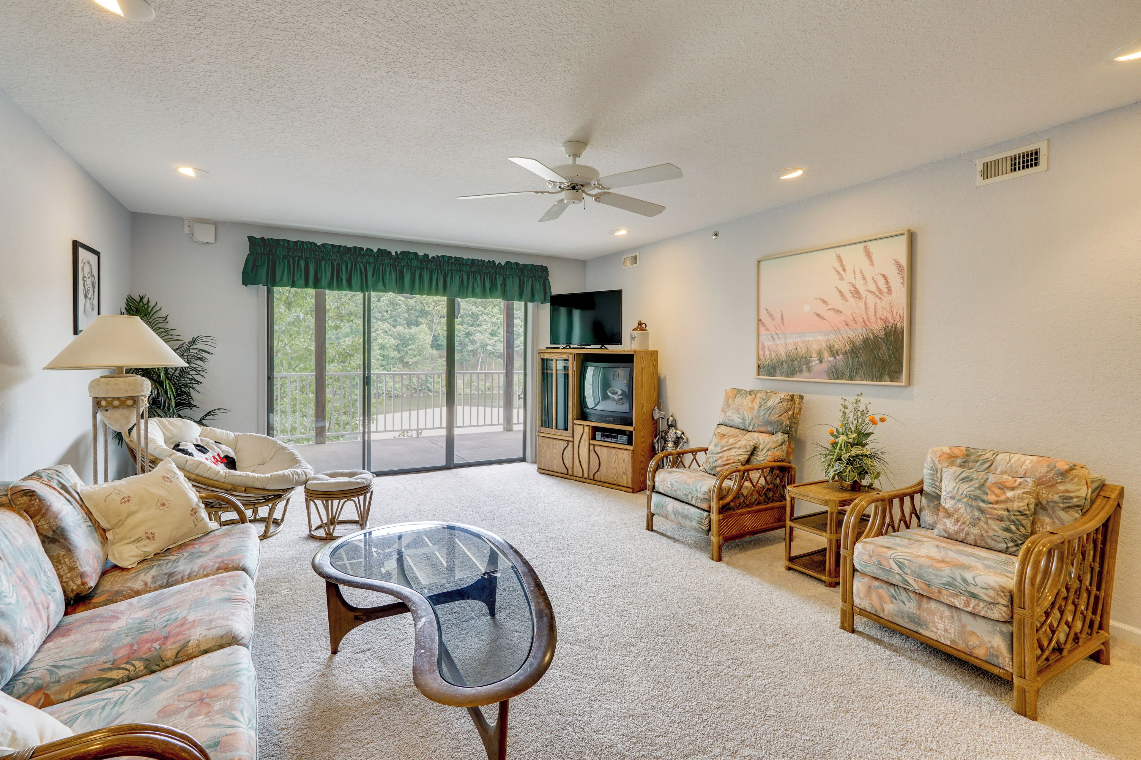 A living room with a sofa, chairs, a television, a ceiling fan, and a large window.
