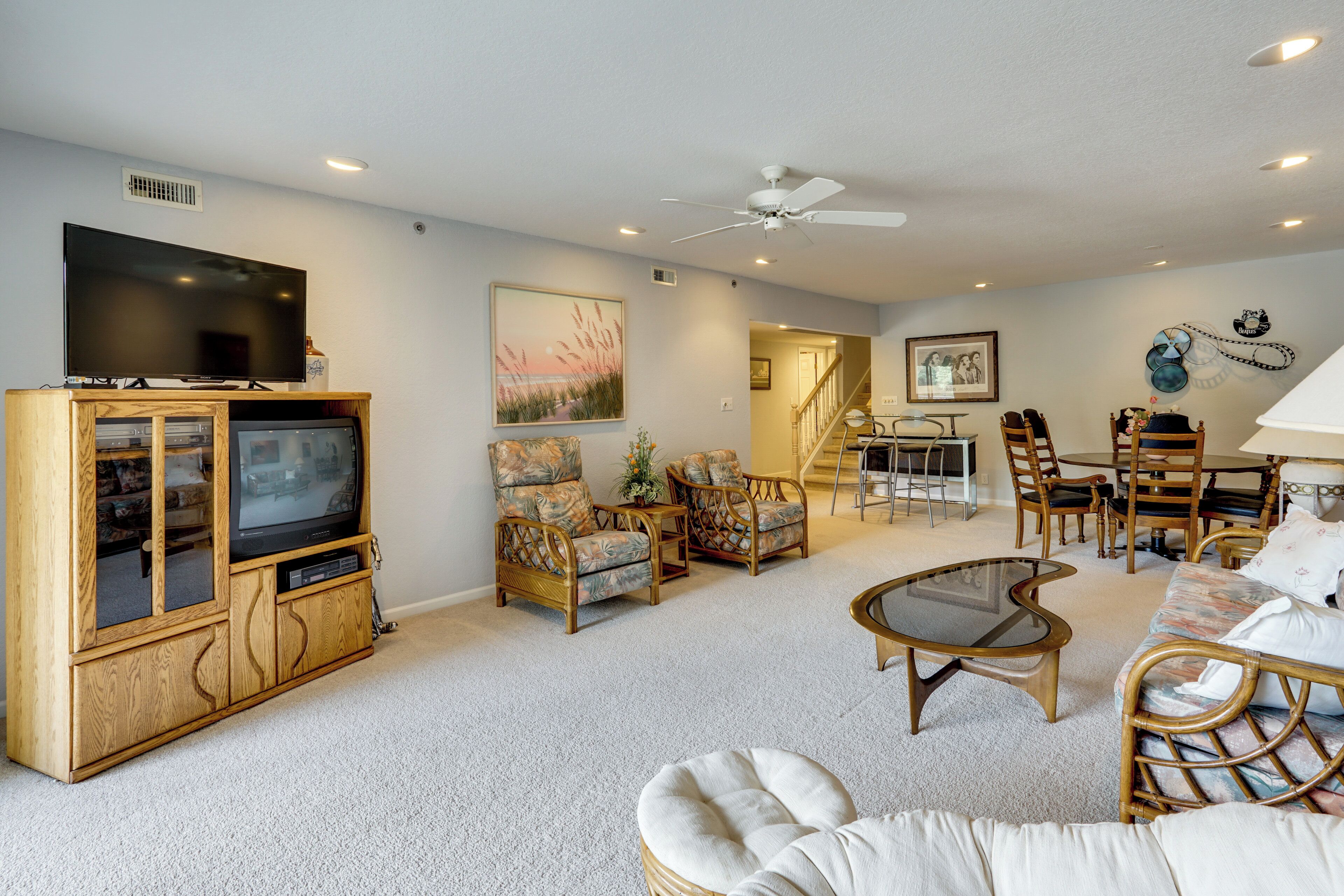 A living room with a TV, wicker furniture, a ceiling fan, and a staircase leading to another level.