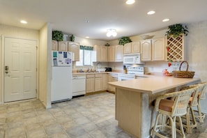A kitchen with light wooden cabinets, a central island with bar stools, a microwave, and a refrigerator. - Tranquil Osage Beach Condo w/ Waterfront Decks! (Osage Beach)