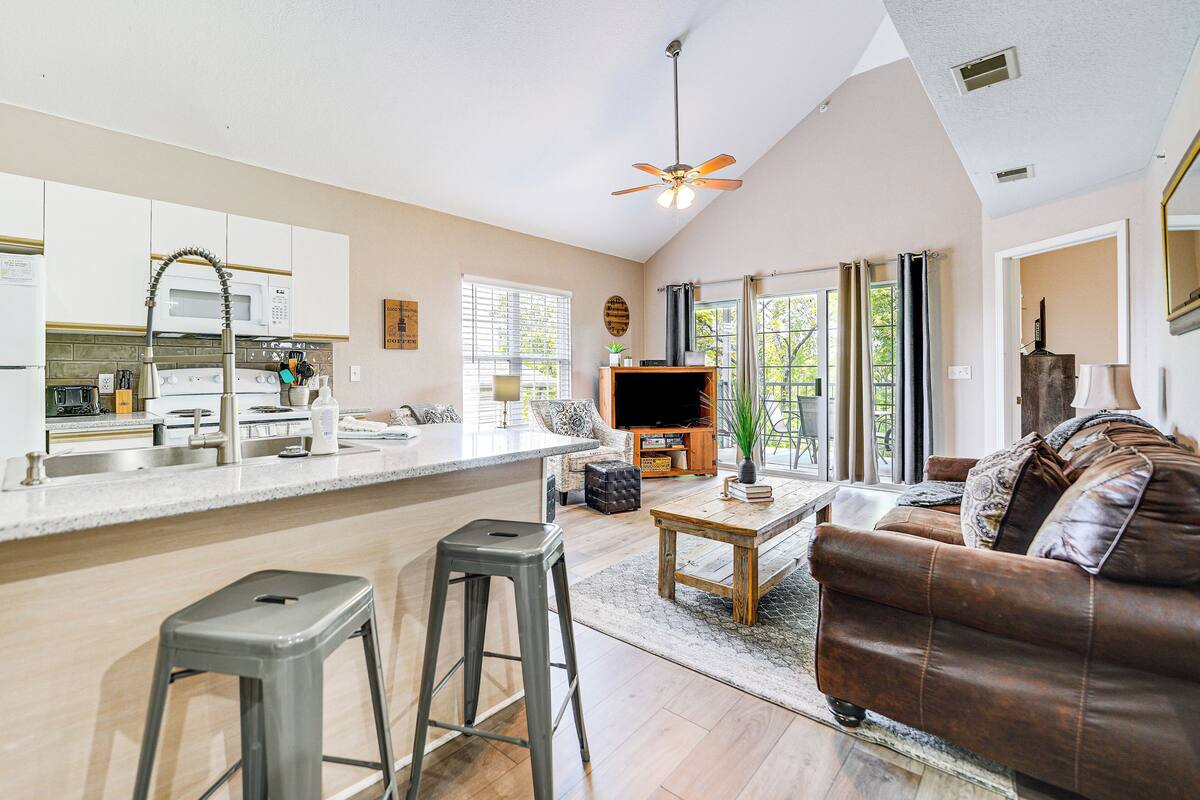 A spacious living area with a kitchen, a brown leather sofa, a wooden coffee table, and a ceiling fan.