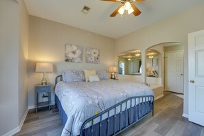 A bedroom with a bed, nightstands, a ceiling fan, and a door leading to another room.