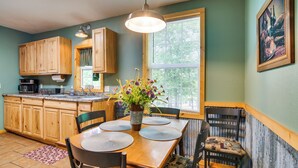 A kitchen with wooden cabinets, a dining table with placemats, a vase with flowers, and a window with blinds. - Bull Shoals Lake Home w/ Porch - Steps to Water! (Cedarcreek)