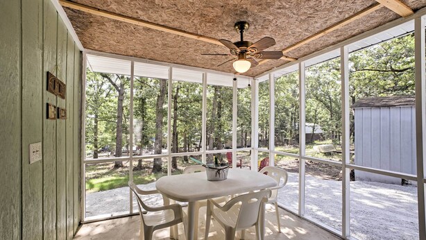 A covered patio with a table and chairs, large windows, and a ceiling fan. - Bull Shoals Lake Home w/ Porch - Steps to Water! (Cedarcreek)