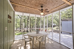 A covered patio with a table and chairs, large windows, and a ceiling fan.