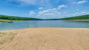 A lake with a pebbly shore and a dock. - Bull Shoals Lake Home w/ Porch - Steps to Water! (Cedarcreek)