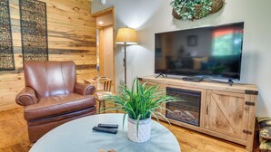 A cozy living room with a leather sofa, a round coffee table with remote controls and wooden coasters, a TV on a wooden cabinet, and a potted plant. - Bull Shoals Lake Home w/ Porch - Steps to Water! (Cedarcreek)