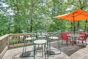 A wooden deck with outdoor furniture, including a table and chairs, surrounded by trees.