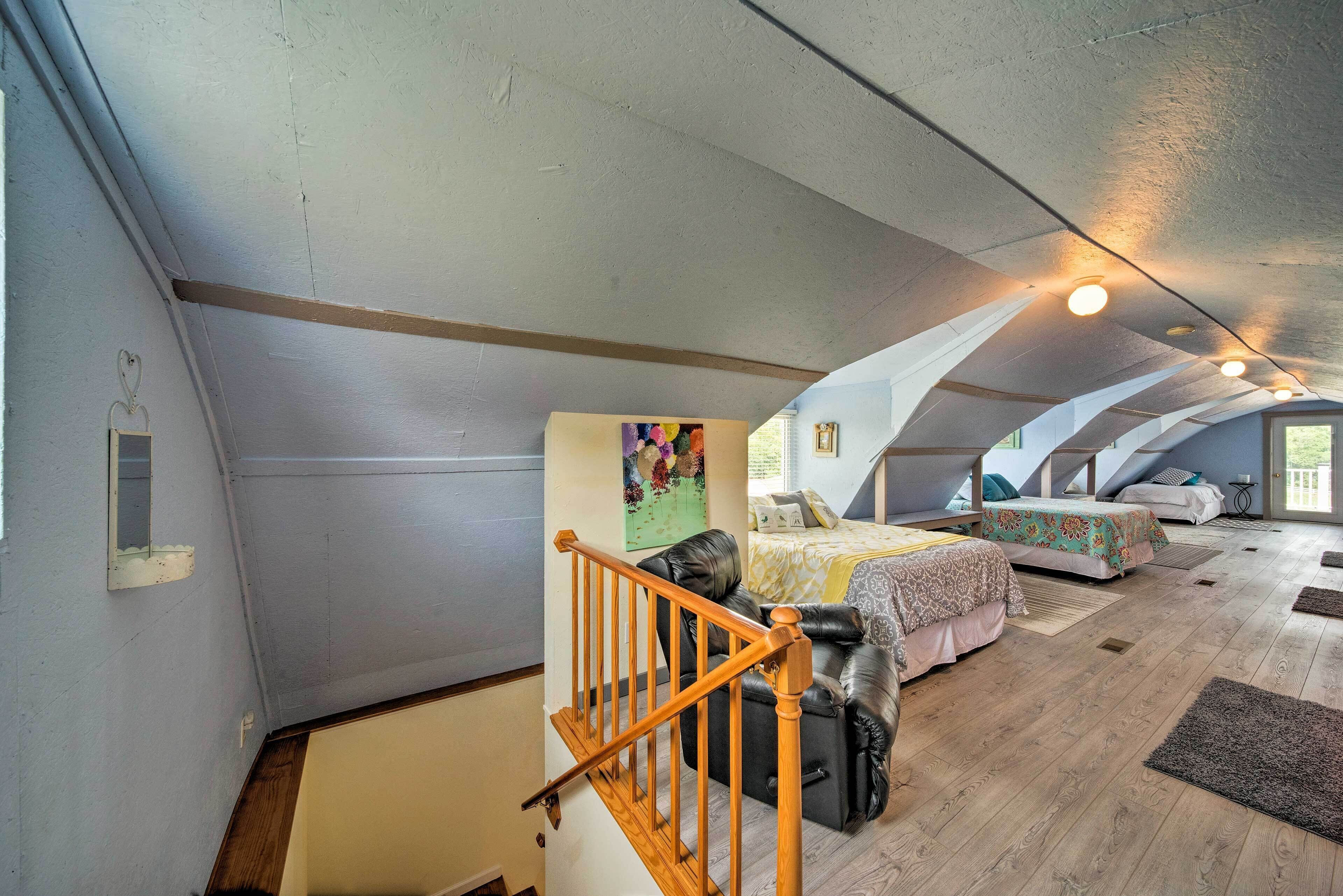 A spacious attic bedroom with a wooden staircase, two beds with colorful bedding, and a large window providing natural light.