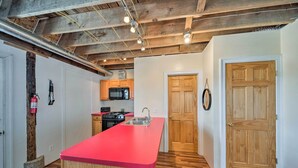 A kitchen with a red countertop, wooden cabinets, a stainless steel sink, and a microwave. There is a wooden door and a white wall with a light switch. - Updated Berger Cottage w/ Pool, on a Private Farm! (Berger)