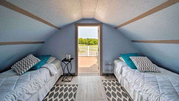 A small attic bedroom with two beds, a window, and a view of a balcony. - Updated Berger Cottage w/ Pool, on a Private Farm! (Berger)