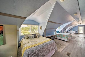A bedroom with a sloped ceiling, a bed with patterned bedding, a window with blinds, and a view of greenery outside. - Updated Berger Cottage w/ Pool, on a Private Farm! (Berger)