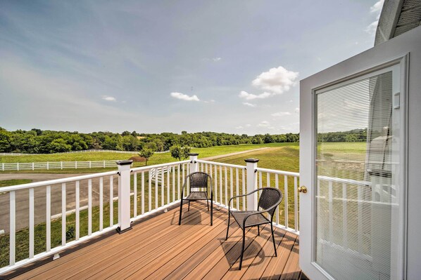 A wooden deck with two chairs and a white railing, overlooking a green landscape with a fence and trees. - Updated Berger Cottage w/ Pool, on a Private Farm! (Berger)