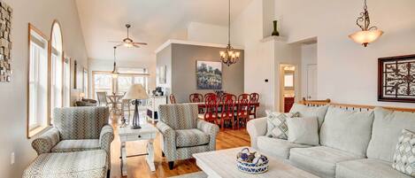 A spacious living room with a large sofa, two patterned armchairs, a coffee table, and a dining area with a red table and chairs.