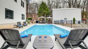 Un jardin avec une piscine, deux chaises longues, une table et un espace barbecue.