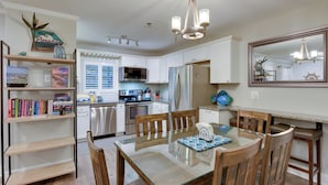 A modern kitchen with white cabinets, a glass dining table, wooden chairs, and a chandelier.