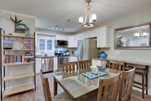 A modern kitchen with white cabinets, stainless steel appliances, a glass dining table, and a chandelier. - Walkable Hilton Head Island Condo w/ Resort Perks (Hilton Head Island)