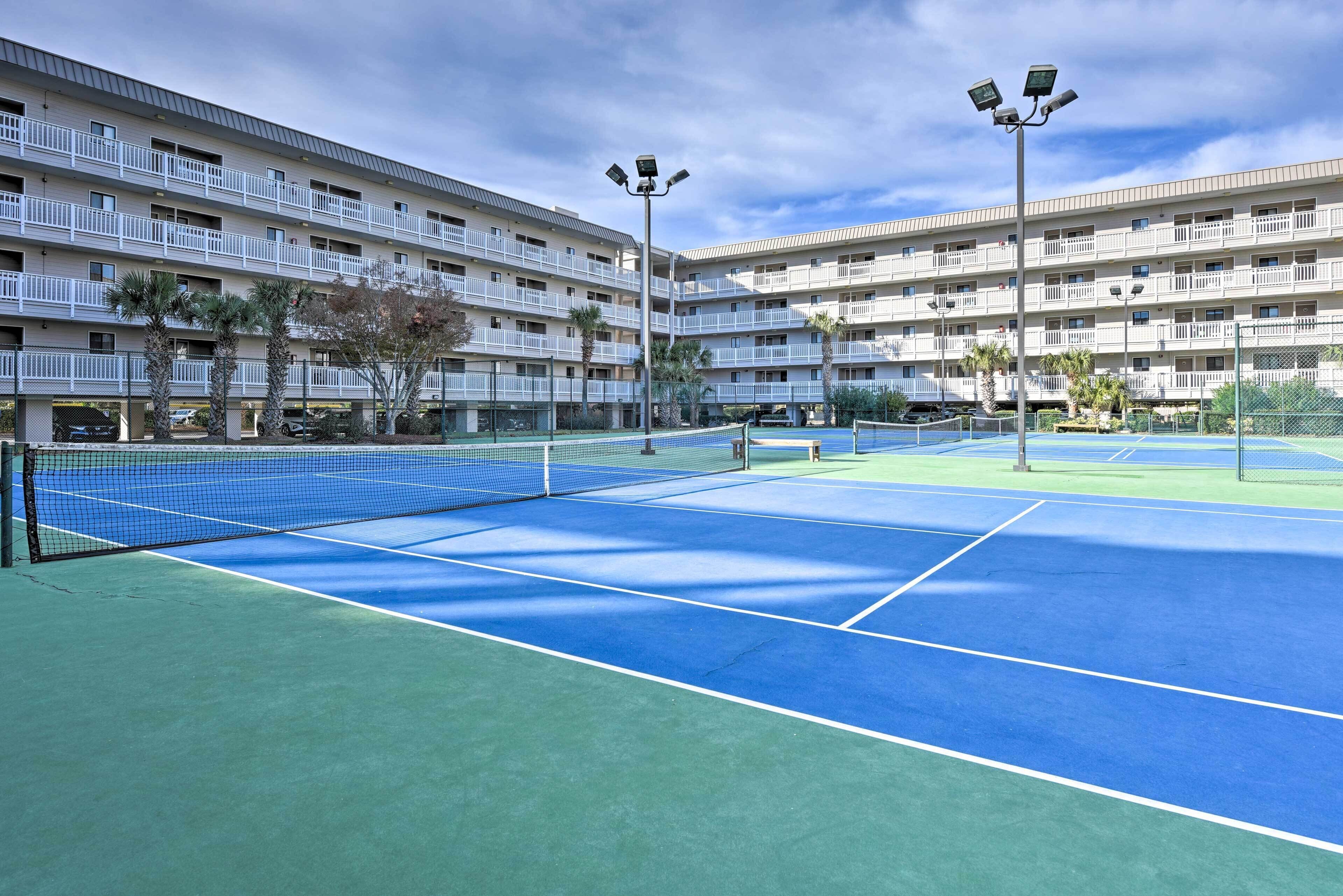 Ein mehrstöckiges Hotel mit Balkonen, Tennisplatz und Palmen.