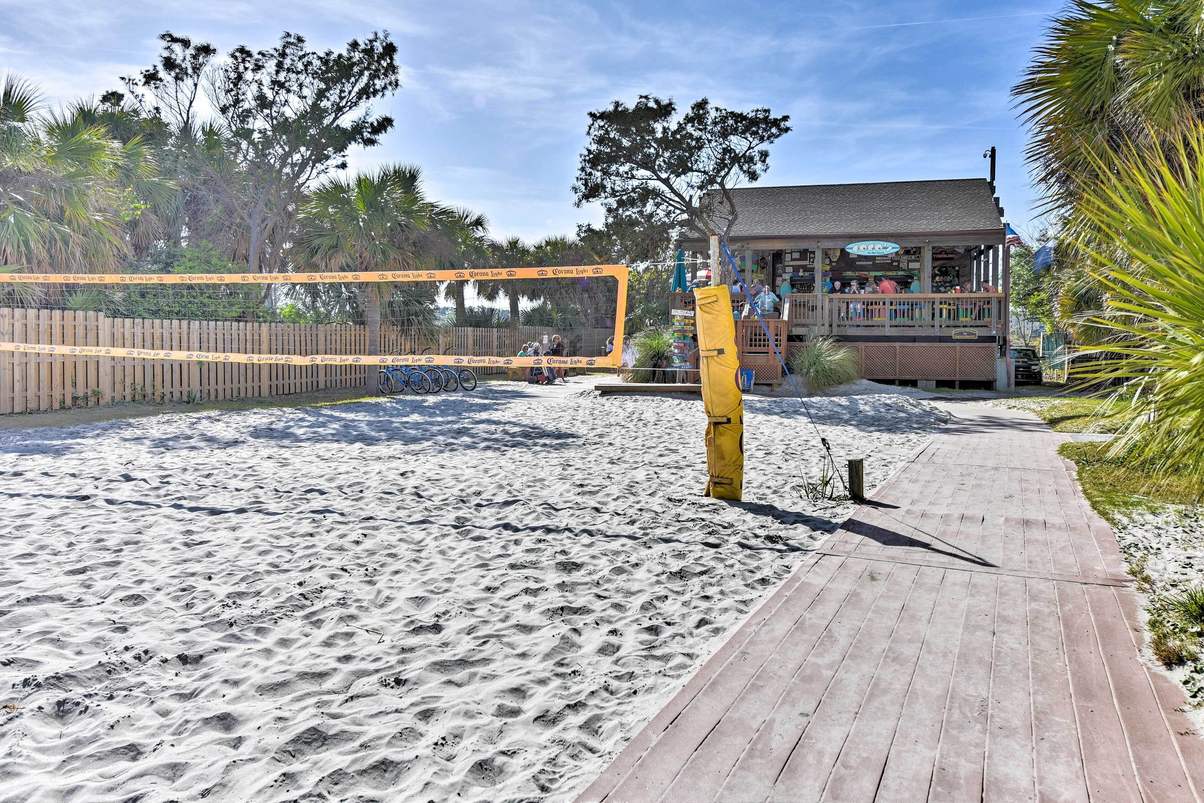 Une plage avec un filet de volley-ball, une promenade en bois et un bâtiment portant une enseigne.
