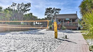 A beach with a volleyball net, a wooden boardwalk, and a building with a sign.