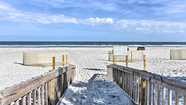 A wooden boardwalk leading to a sandy beach with a clear sky.