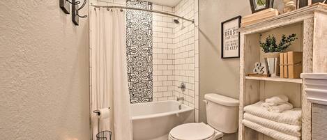 A bathroom with a bathtub, toilet, and a shelf with towels.