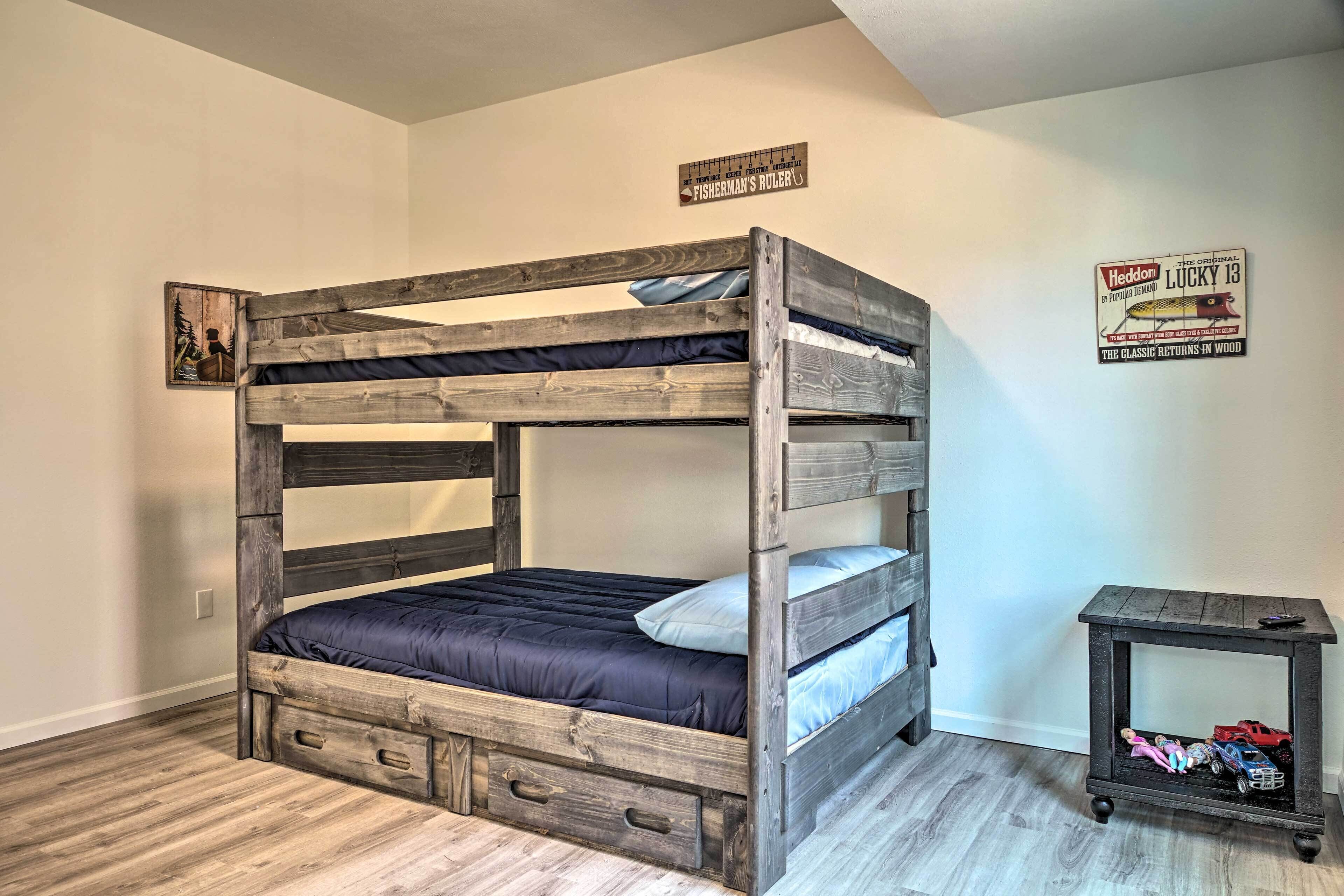 A bunk bed with drawers at the foot, a small table with toys, and a poster on the wall.