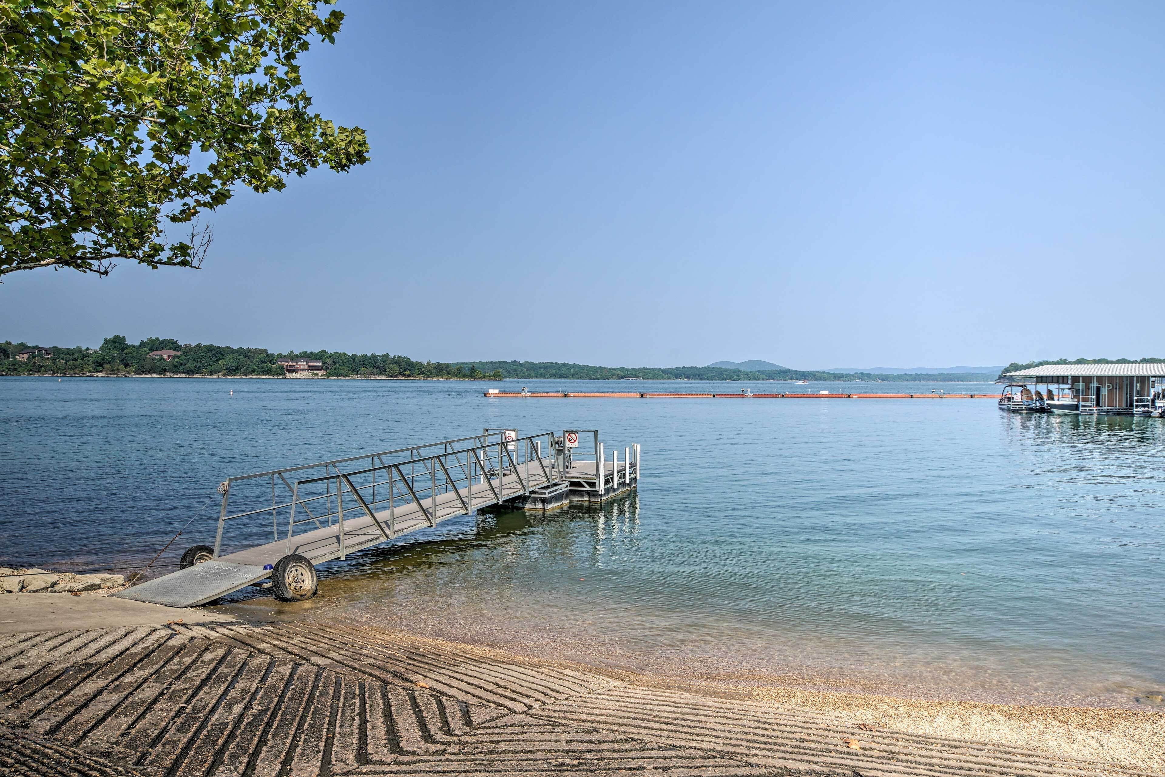 A calm lake with a dock extending into the water, surrounded by trees and a distant shoreline.