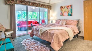 A bedroom with a large bed, a sliding glass door leading to a balcony, a ceiling fan, and a painting on the wall.