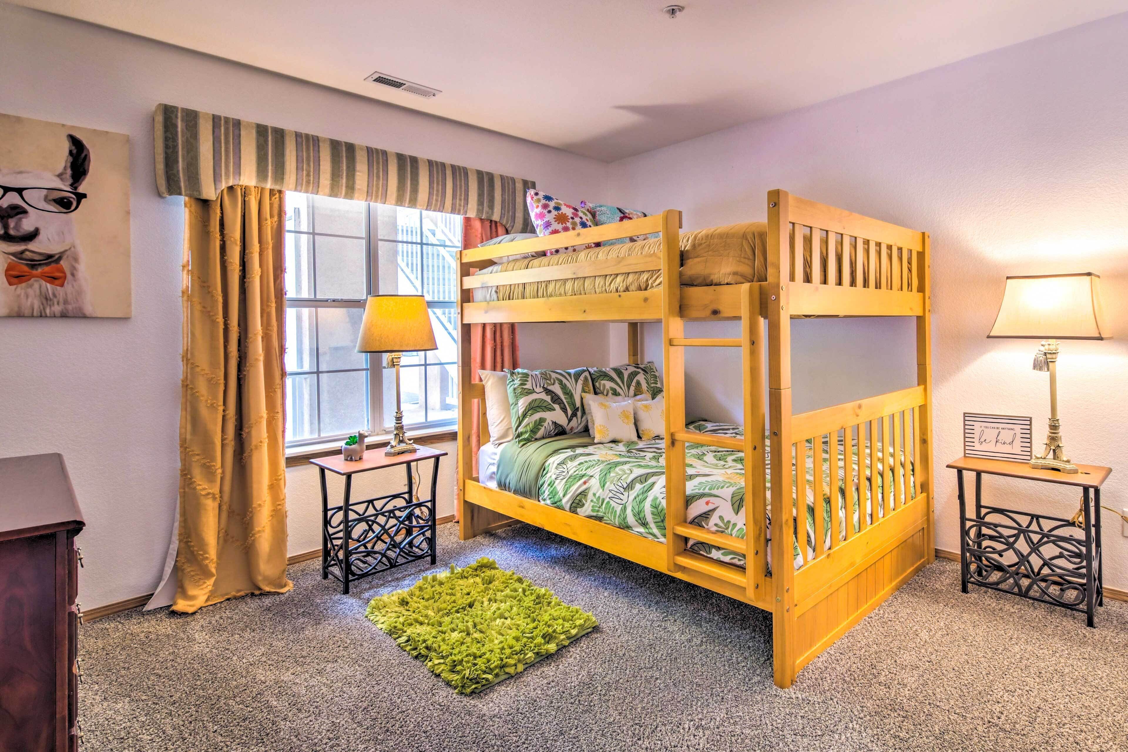 A bunk bed with a green leaf-patterned bedspread, a small table with a lamp, and a green rug on a carpeted floor.