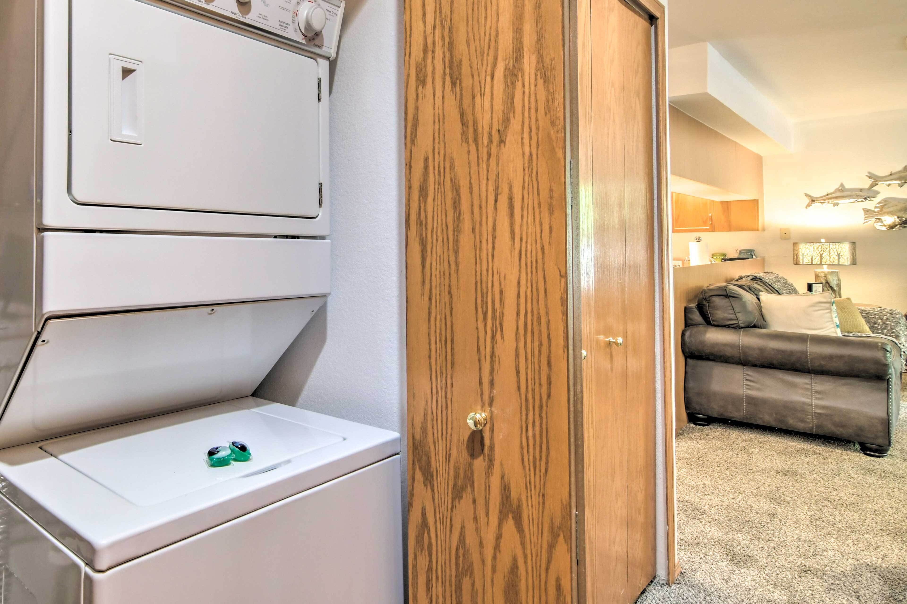 Un área de lavandería con lavadoras y secadoras apiladas, una puerta de madera y una sala de estar con un sofá y una lámpara.
