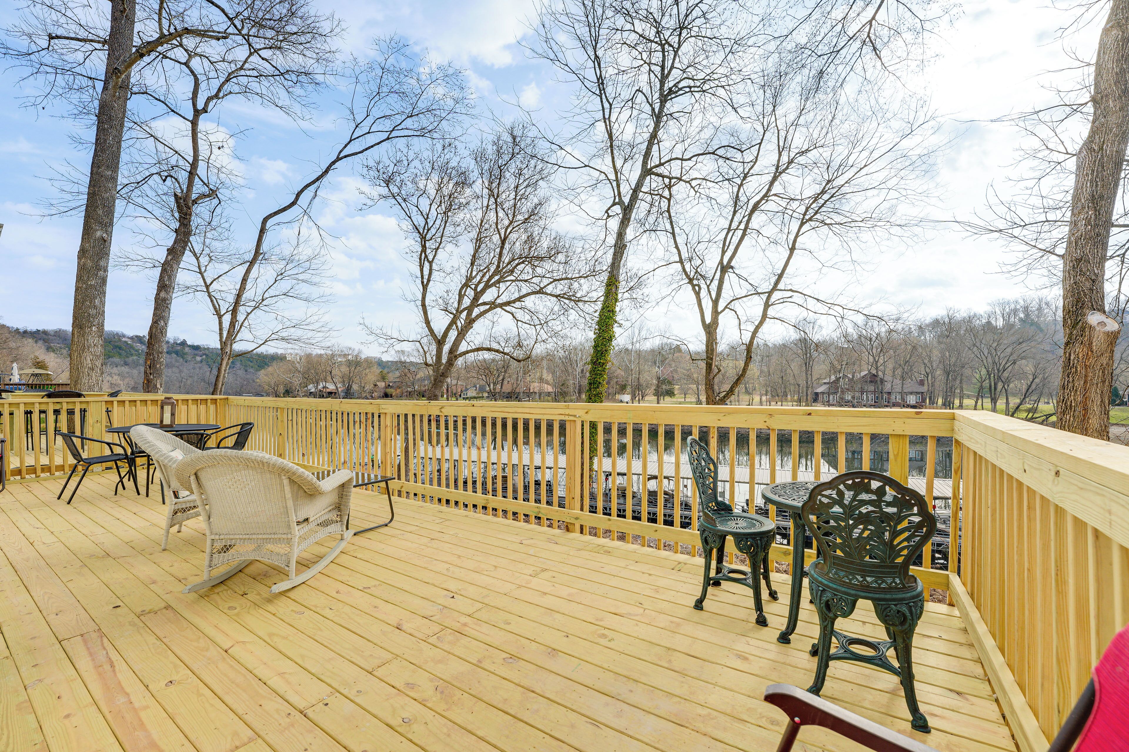 A wooden deck with outdoor furniture, including a rocking chair and chairs, overlooking a body of water and trees.