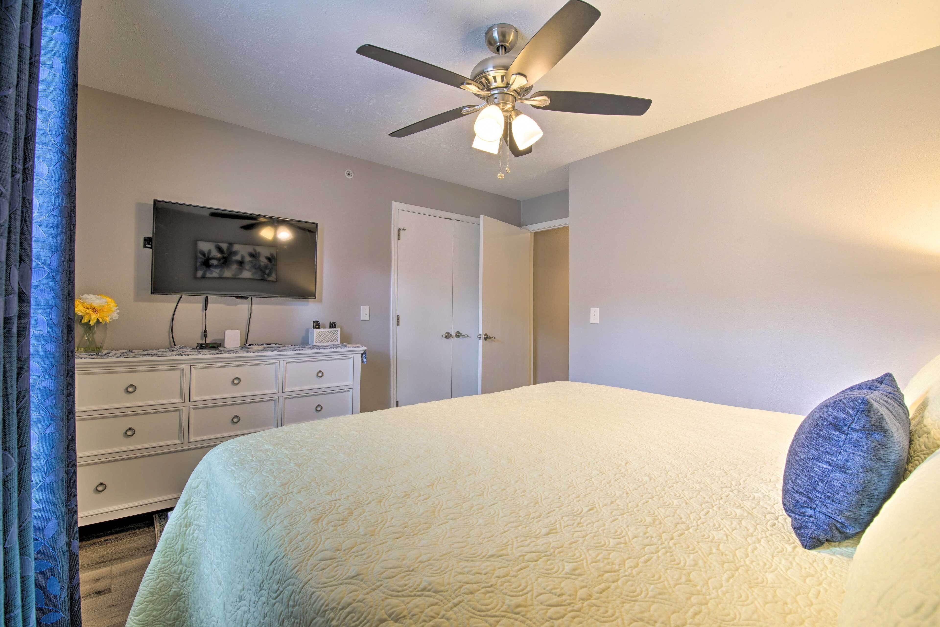 A bedroom with a bed, a ceiling fan, a TV, a dresser, and a door.