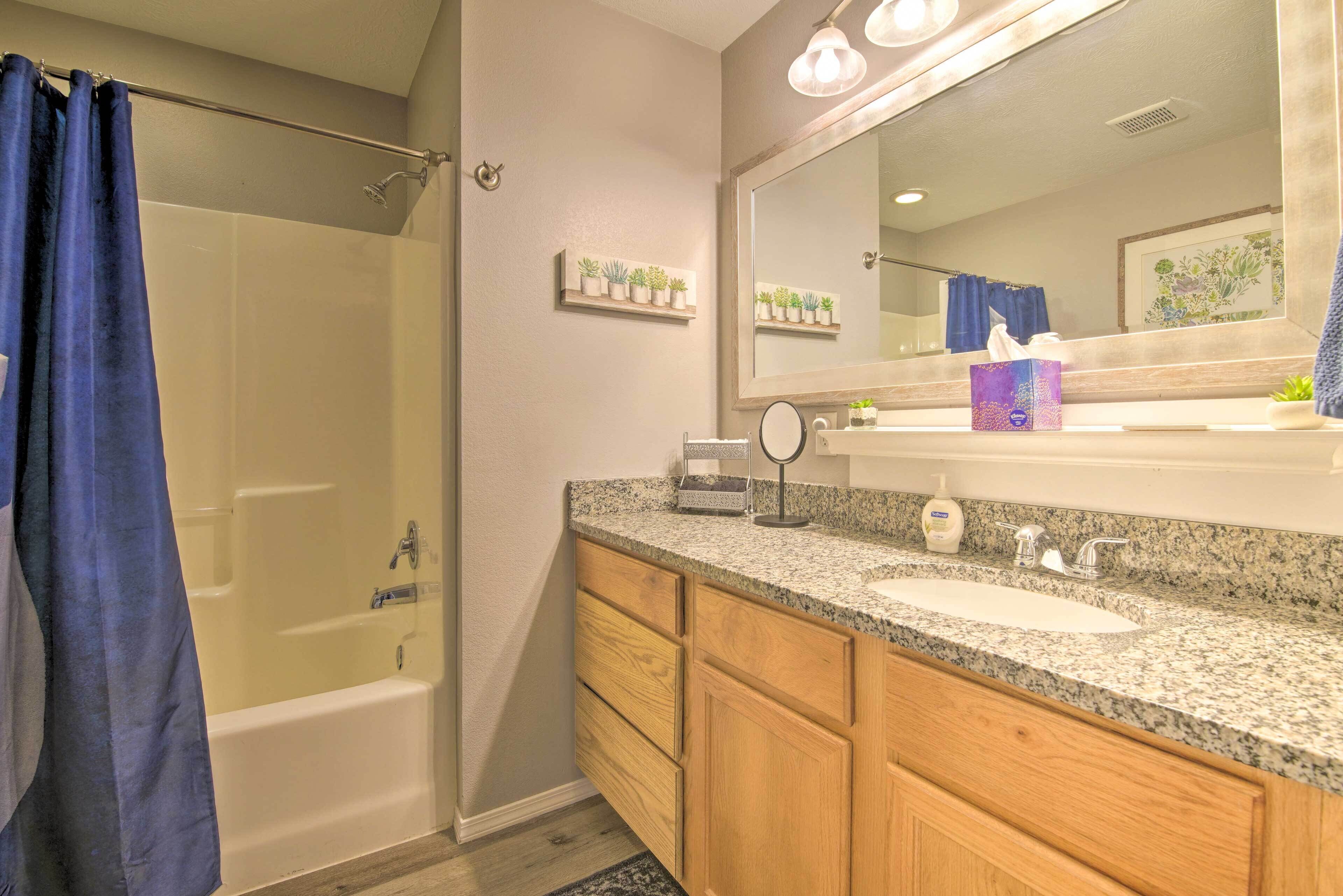 A modern bathroom with a bathtub, two sinks, wooden cabinets, a vanity mirror, and a shower curtain.