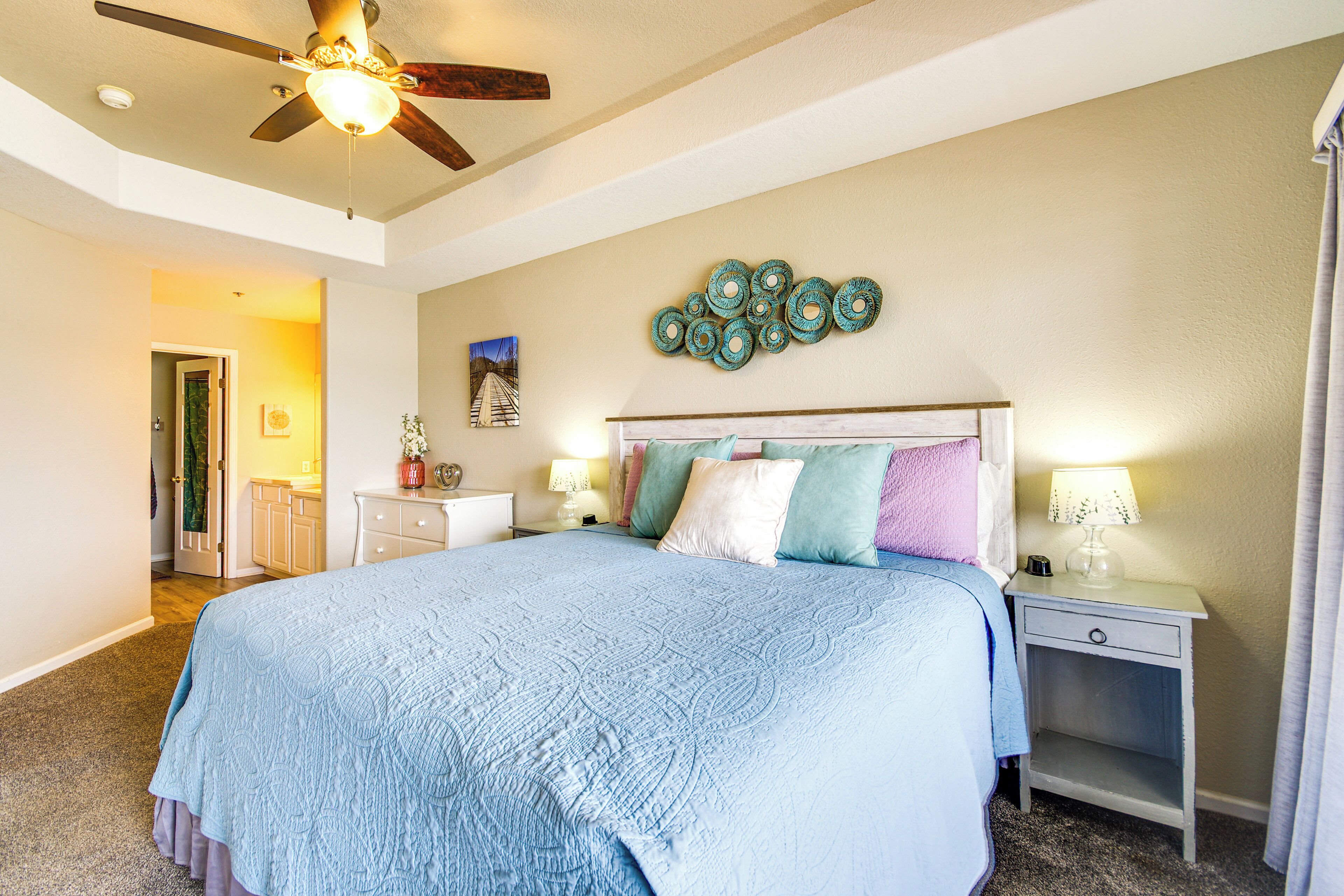 A bedroom with a bed, nightstands, a ceiling fan, and a wall decoration.