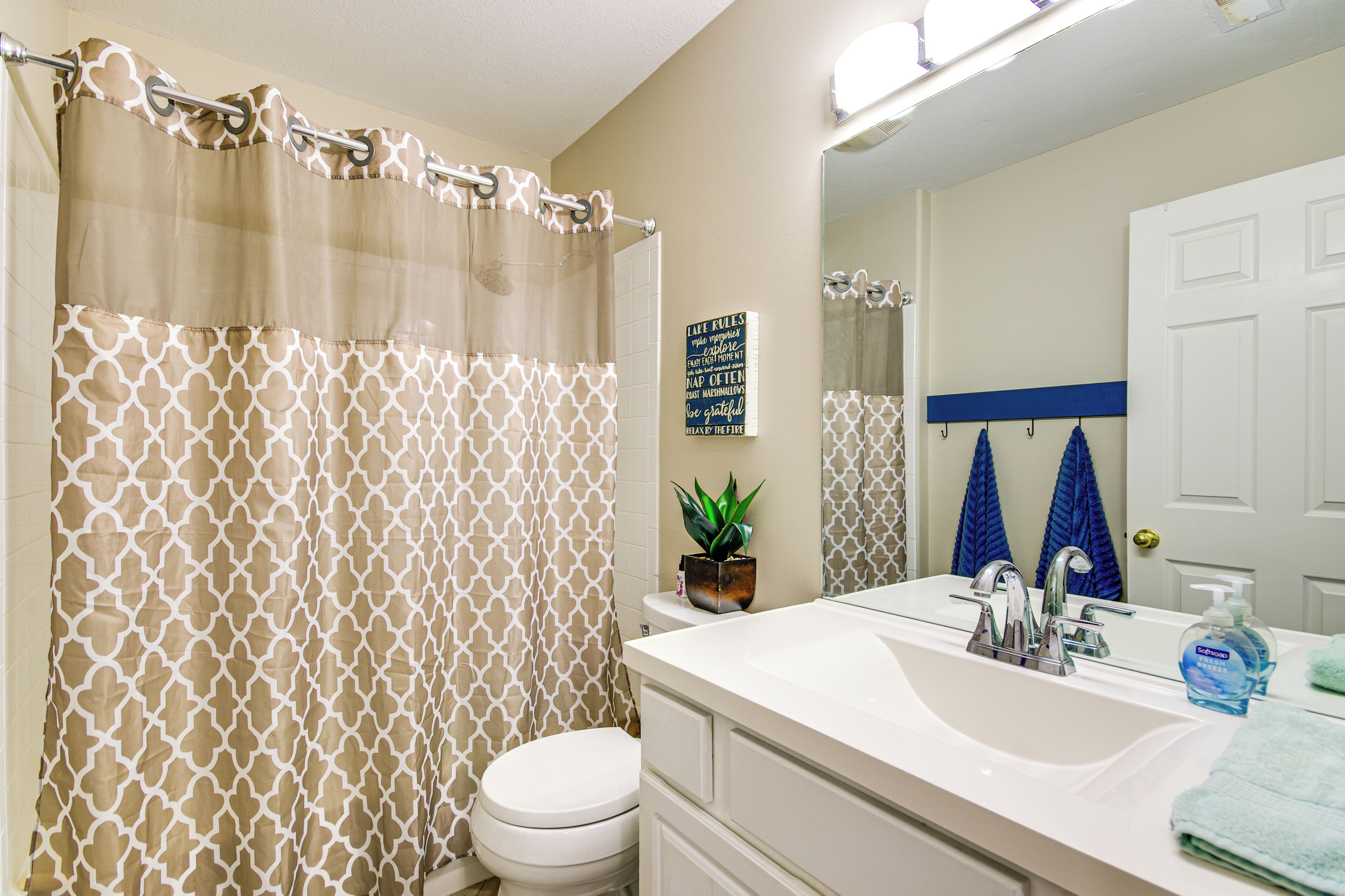 A bathroom with a toilet, sink, and shower curtain. There is a potted plant on the sink counter and a towel rack with towels.