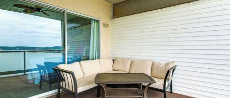 Een balkon met een rieten tafeltje en een comfortabele zithoek, met uitzicht op een waterpartij.