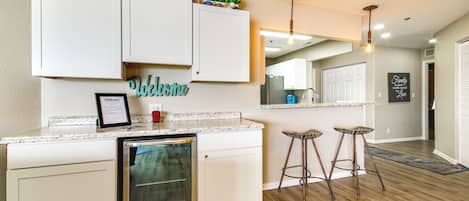 Una cocina con armarios blancos, lavavajillas integrado y un letrero de bienvenida.