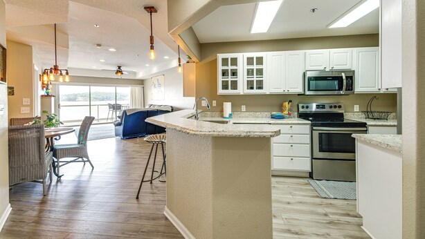 A modern kitchen with white cabinets, a central island, stainless steel appliances, and a dining area with wicker furniture. - Community Perks! Waterfront Lake Ozark Escape (Lake Ozark)