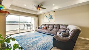 A spacious living room with a large window, a ceiling fan, and a map on the wall. - Community Perks! Waterfront Lake Ozark Escape (Lake Ozark)