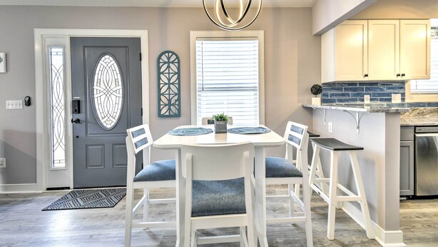 A dining area with a white table and chairs, a chandelier, and a kitchen with light-colored cabinets. - Updated Myrtle Beach Cottage w/ Shared Pool! (Myrtle Beach)