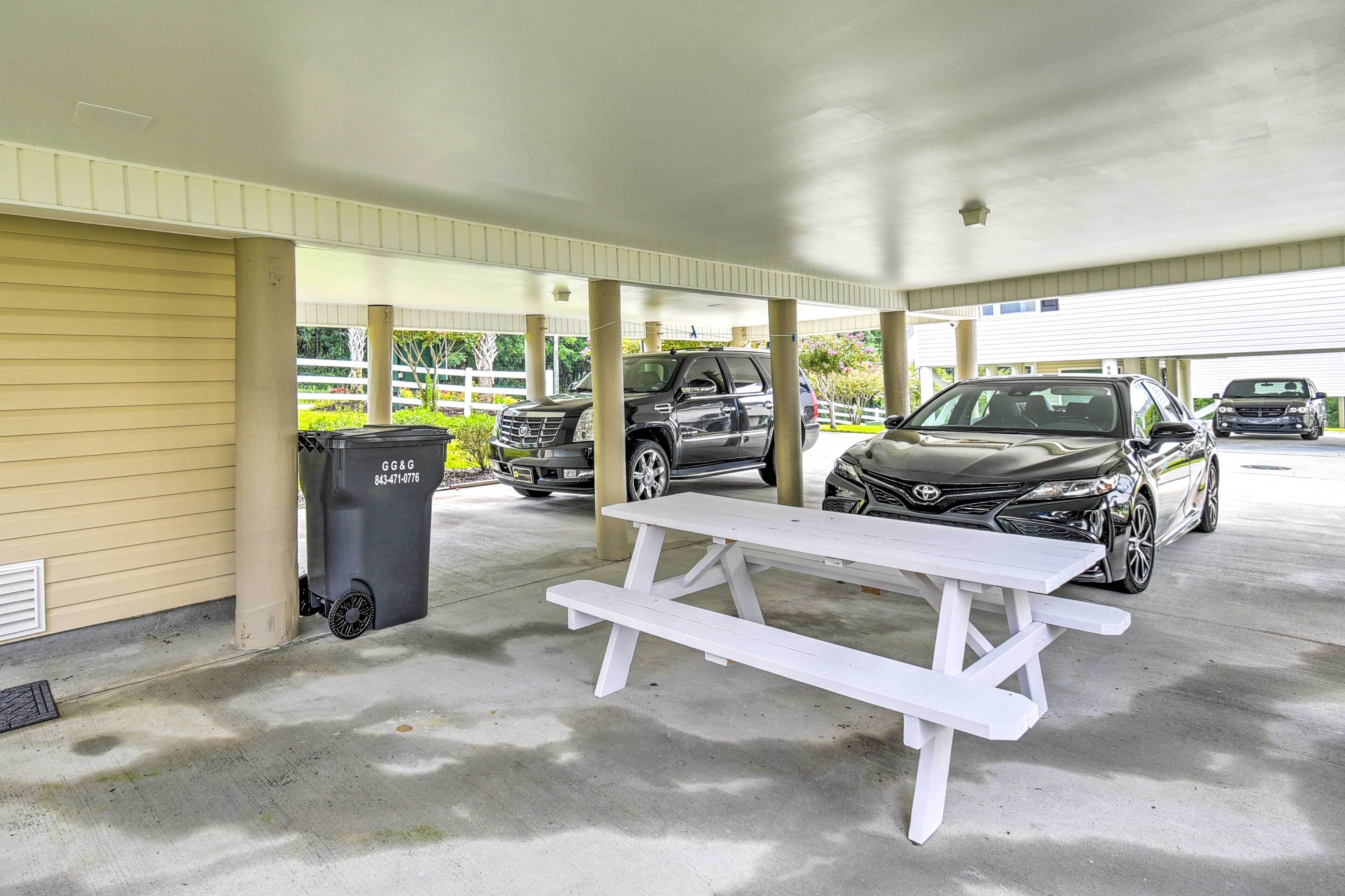 A covered parking area with a picnic table and a trash bin.