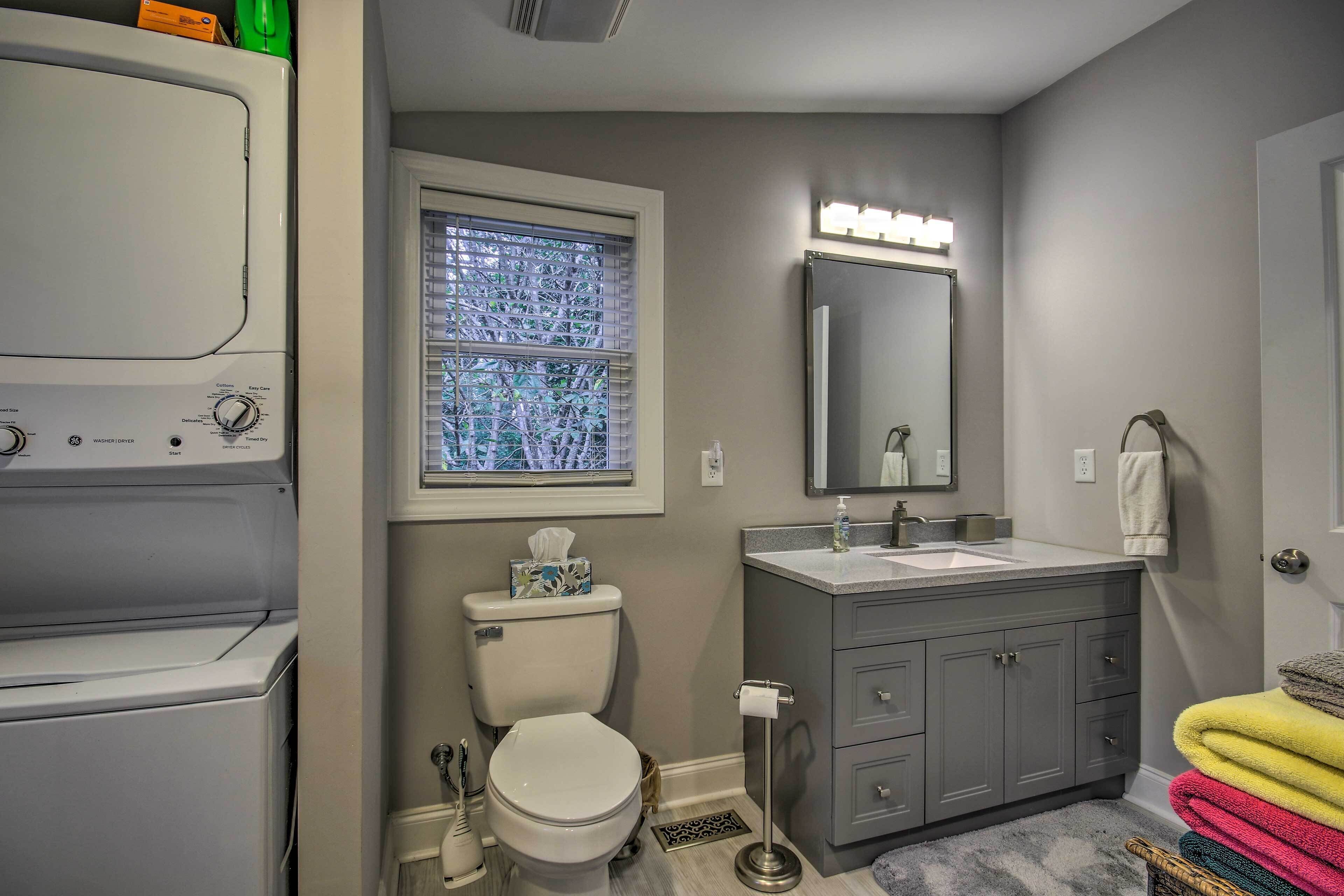 A bathroom with a washing machine, toilet, sink, and a window with blinds.