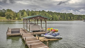 A wooden dock with a covered seating area, a jet ski, and colorful floating toys. - Waterfront Greenwood Getaway w/ Deck & Grill! (Greenwood)