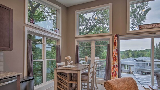 A dining area with a wooden table and chairs, large windows with curtains, and a view of the outside. - Waterfront Greenwood Getaway w/ Deck & Grill! (Greenwood)