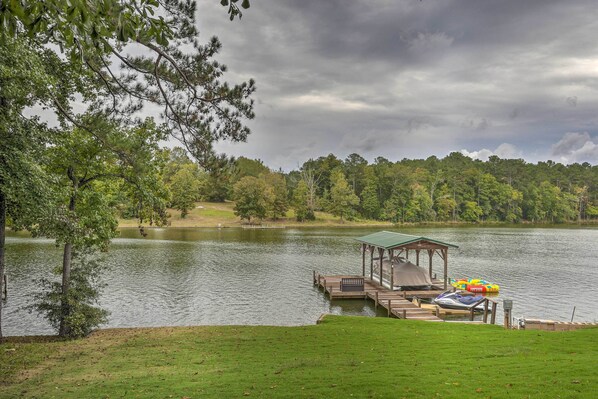 Um cais à beira do lago com um gazebo, um jet ski e bóias infláveis.