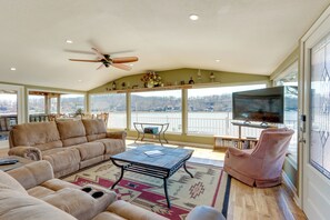 Un salon spacieux avec un grand canapé, une table basse et un téléviseur. Il y a un balcon avec vue sur l’extérieur.