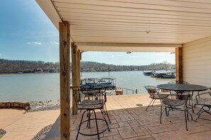 A covered patio with outdoor seating and a view of a lake and boats.
